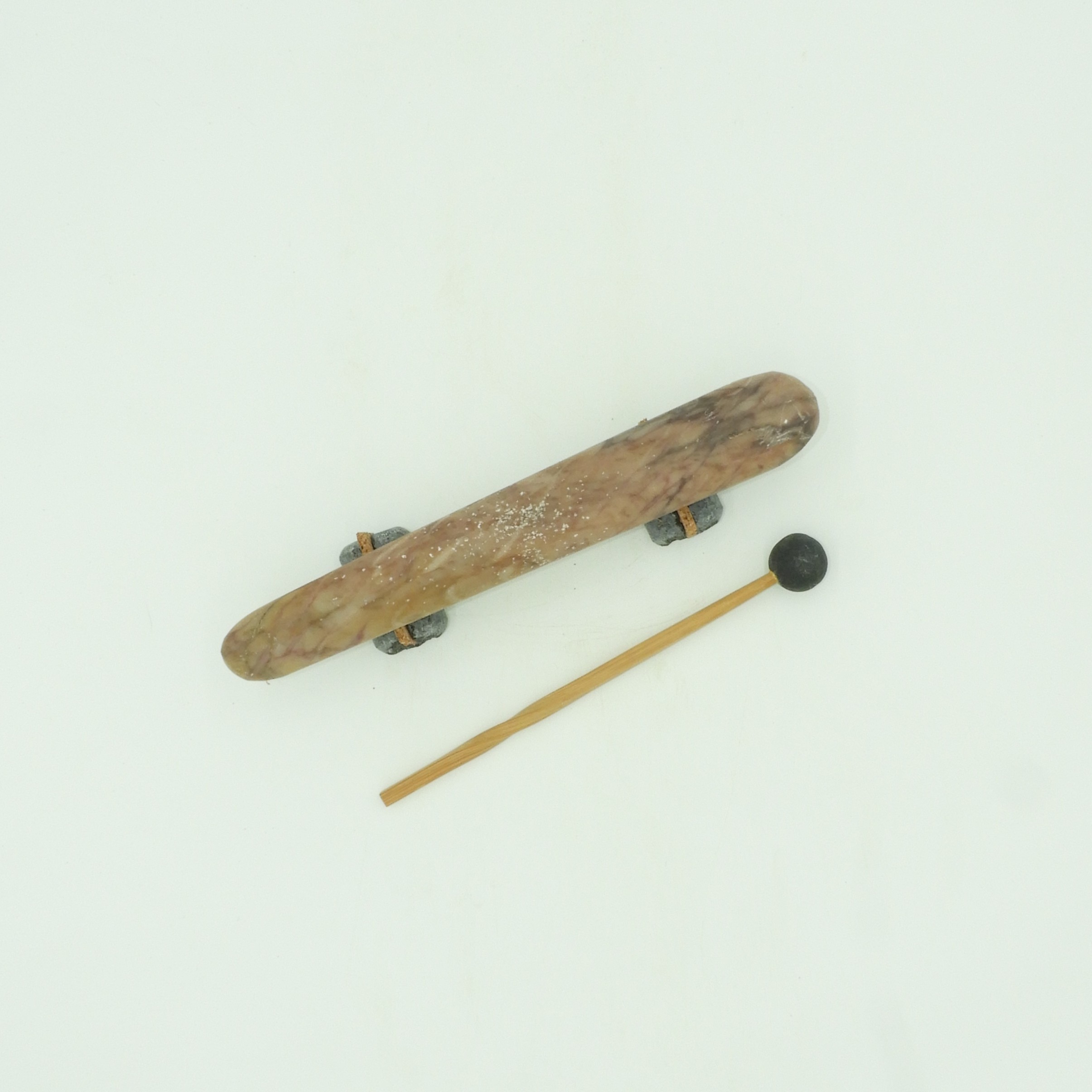 Reproducción artesanal de los primeros instrumentos de percusión de la humanidad: un litófono de piedra natural, mármol morado con veta sobre soportes de mármol negro con corcho natural y baqueta de madera con esfera de granito negro.